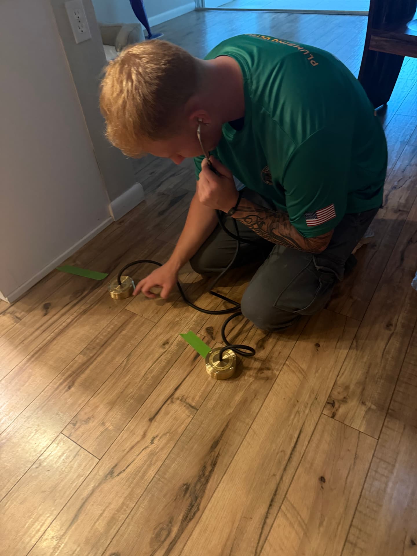Technician listening with geophone discs on a wood floor to pinpoint the leak
